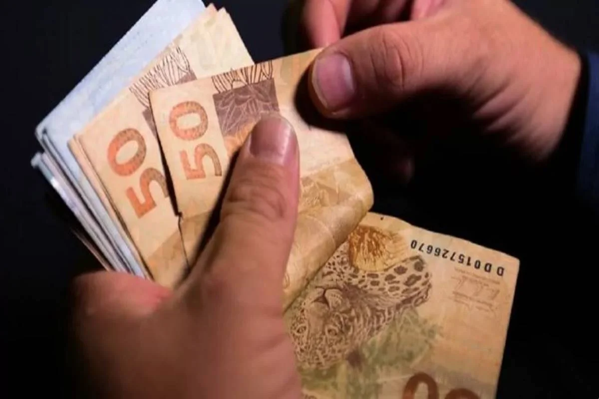 foto colorida de duas mãos segurando um maço de dinheiro PIS Pasep e referente ao abono salarial