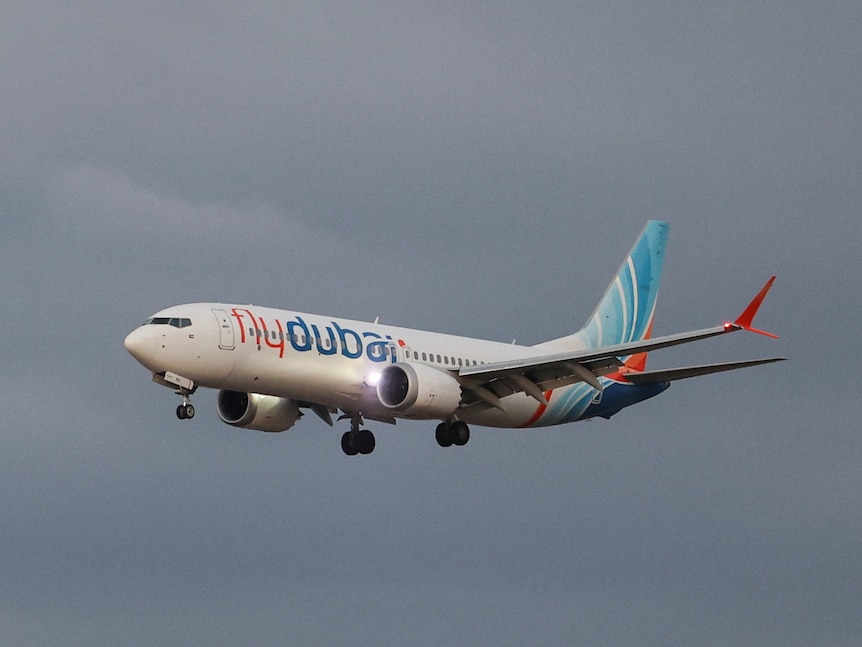 A white, blue and orange flydubai Boeing 737 aircraft flies against an overcast sky